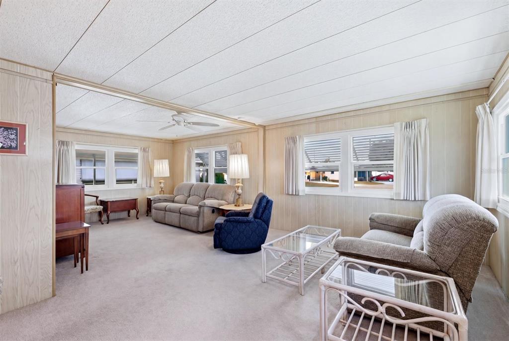 A living room with beige wood-paneled walls, light carpeting, and several pieces of upholstered furniture — 4203 11TH STREET COURT E, ELLENTON, FL