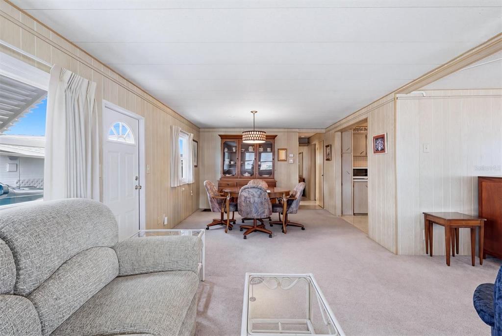 A living and dining area with wood-paneled walls, beige carpeting, and a wooden china cabinet — 4203 11TH STREET COURT E, ELLENTON, FL