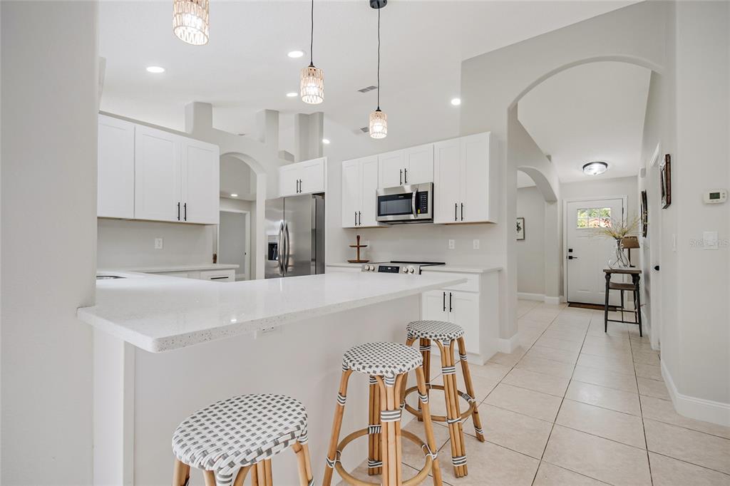 A bright kitchen features white cabinets, stainless steel appliances, a quartz island, and rattan stools — 4040 EAGLE FEATHER DRIVE, ORLANDO, FL