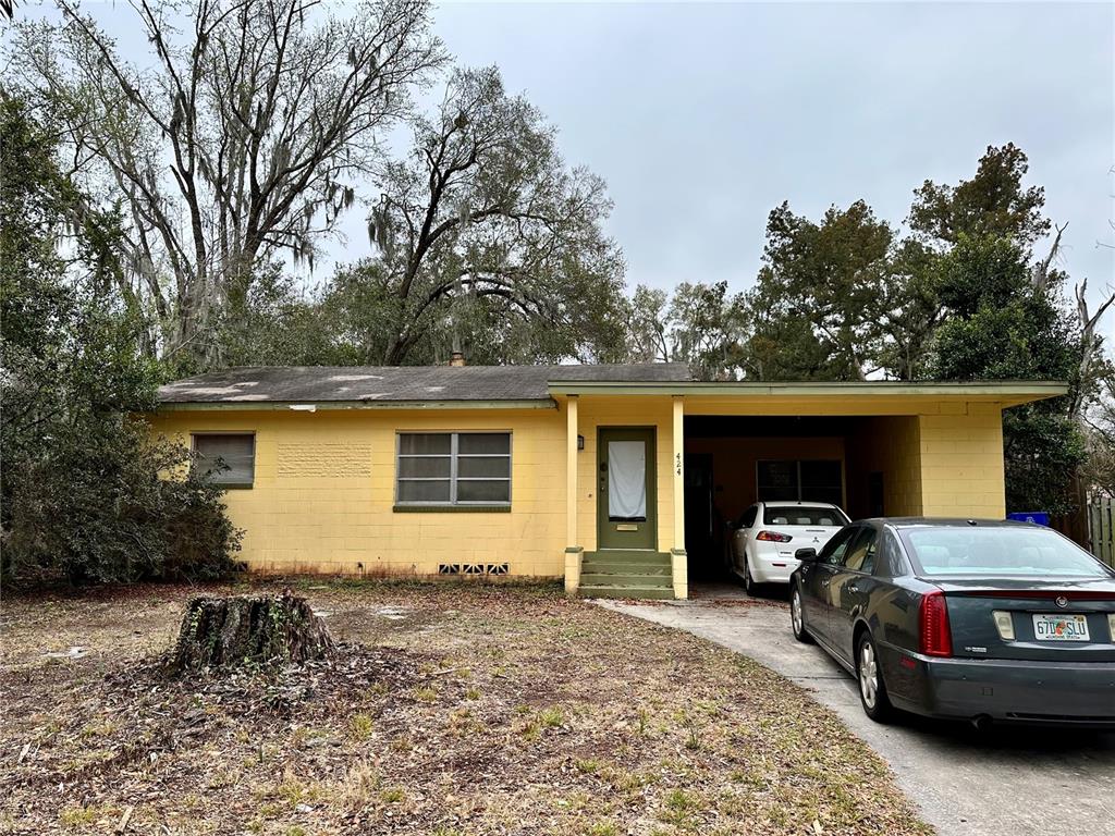 A yellow, single-story concrete block house with a carport and a front yard tree stump — 424 W HOGLE AVENUE, DELAND, FL