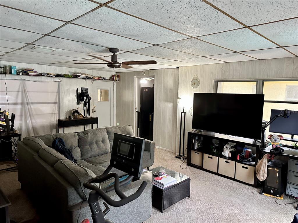 A living room features a gray sectional sofa, exercise bike, large television, and drop ceiling — 424 W HOGLE AVENUE, DELAND, FL