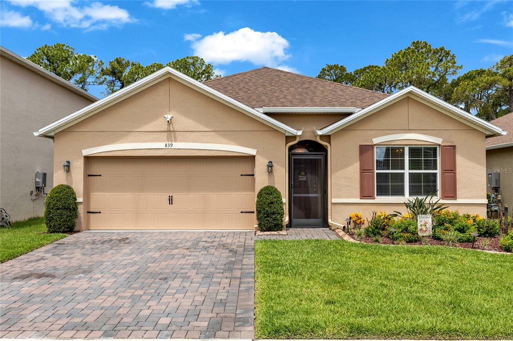 A single-story tan house with a two-car garage, brick driveway, and a front garden — 839 LAZIO CIRCLE, DEBARY, FL