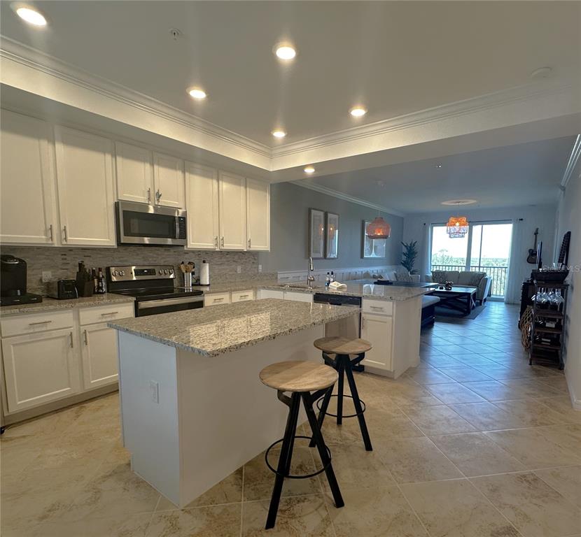A kitchen with white cabinets, granite countertops, and an island with two stools — 14091 HERITAGE LANDING BOULEVARD UNIT 134, PUNTA GORDA, FL