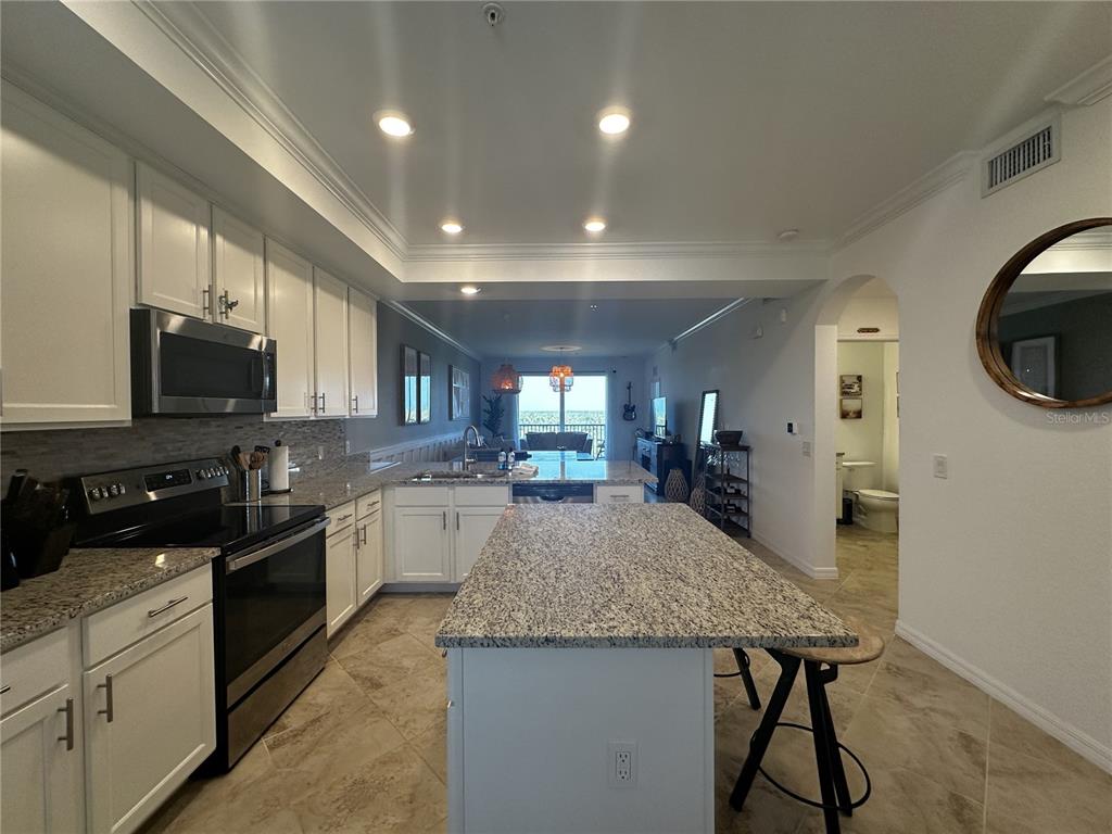 A kitchen with white cabinets, granite countertops, and a central island overlooks an open living area — 14091 HERITAGE LANDING BOULEVARD UNIT 134, PUNTA GORDA, FL