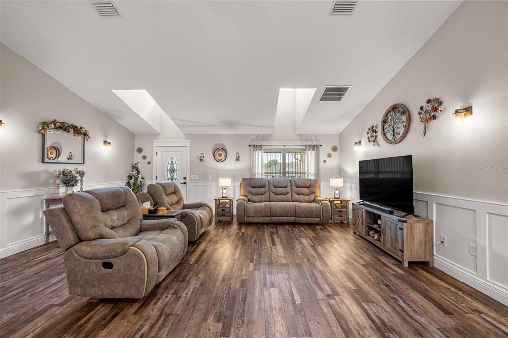A living room features wood-look flooring, white wainscoting, vaulted ceilings with skylights, and gray furniture — 6658 SW 109TH LANE, OCALA, FL