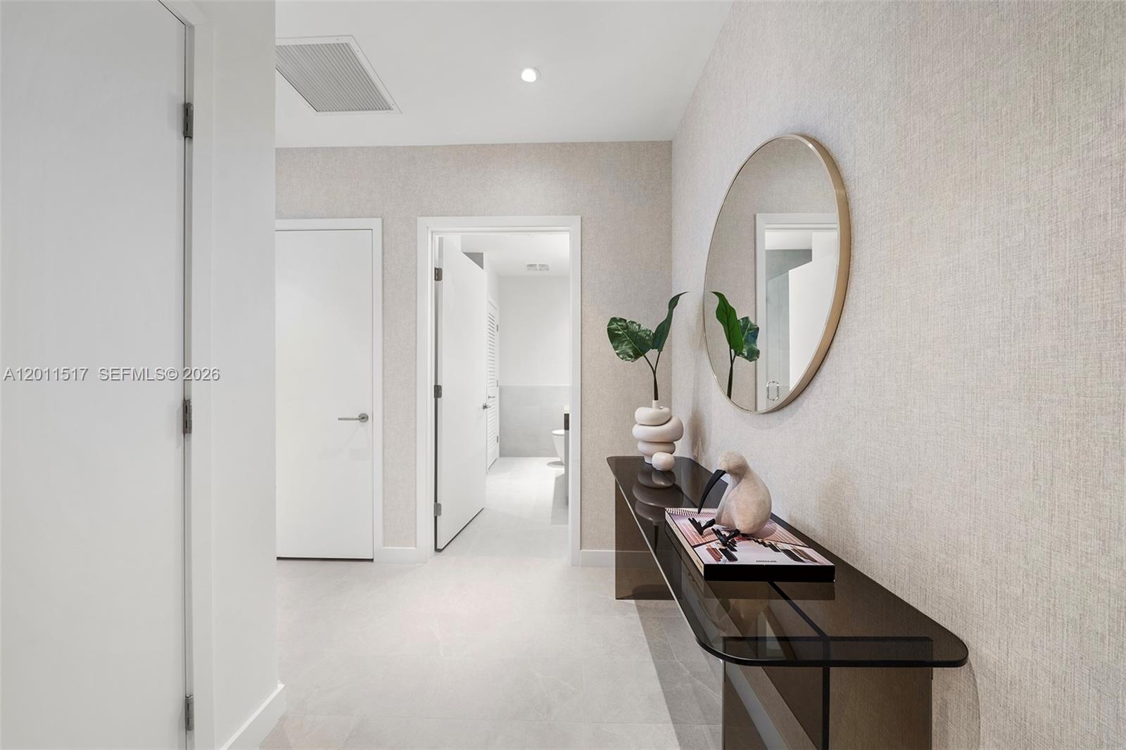 A hallway features light-colored textured wallpaper, a glass console table, and a round wall mirror — 500 Alton Rd # 501, Miami Beach FL 33139, MIAMI BEACH, FL