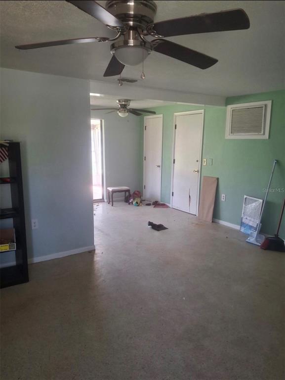 An interior view of a room with concrete floors, two ceiling fans, and green walls — 4601 EASTWOOD LANE, HOLIDAY, FL