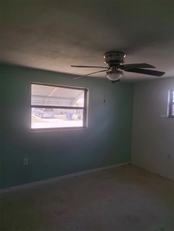 A bedroom with light green walls, a ceiling fan, and a window overlooking a carport — 4601 EASTWOOD LANE, HOLIDAY, FL