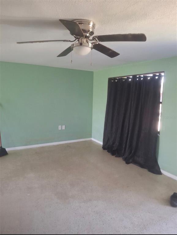 An empty room with green walls, beige carpeting, a ceiling fan, and black window curtains — 4601 EASTWOOD LANE, HOLIDAY, FL