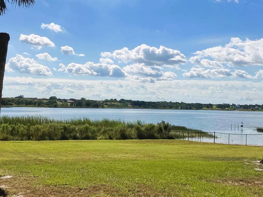 A grassy lawn overlooks a lake with a fence and distant shoreline under a cloudy sky — 1854 HIGHLAND PARK DRIVE S UNIT A-F, LAKE WALES, FL
