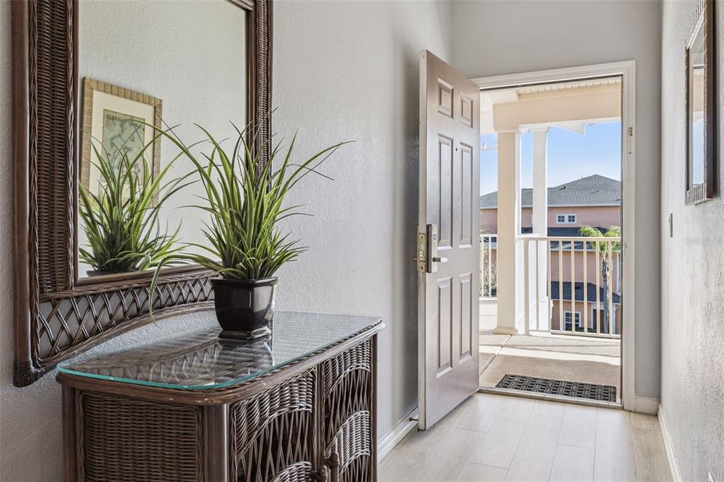 An entryway features a wicker console table, a mirror, and an open door to a balcony — 714 NEW PROVIDENCE PROMENADE, DAVENPORT, FL