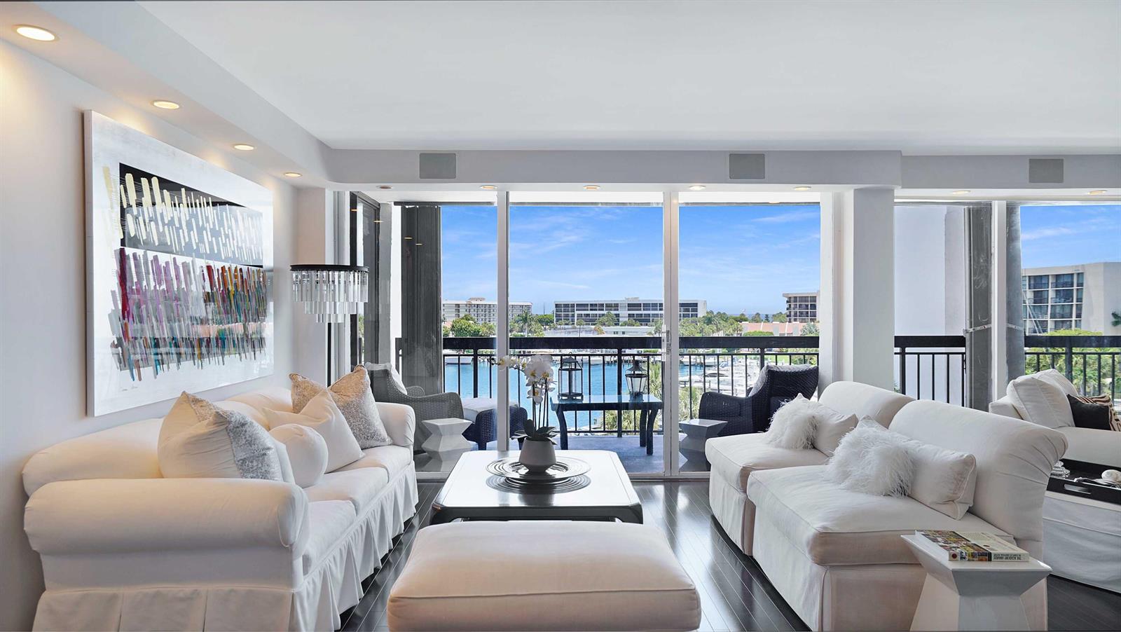 A living room features white sofas, a dark coffee table, and floor-to-ceiling windows overlooking water — 2697 N Ocean Boulevard # 505, Boca Raton FL 33431, BOCA RATON, FL