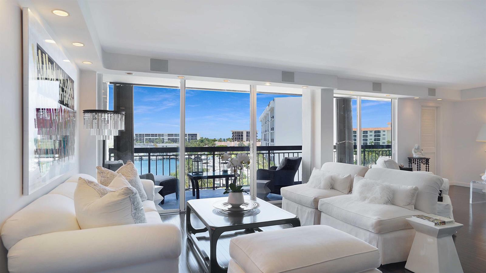 A bright living room features white furniture, a coffee table, and sliding glass doors overlooking water — 2697 N Ocean Boulevard # 505, Boca Raton FL 33431, BOCA RATON, FL