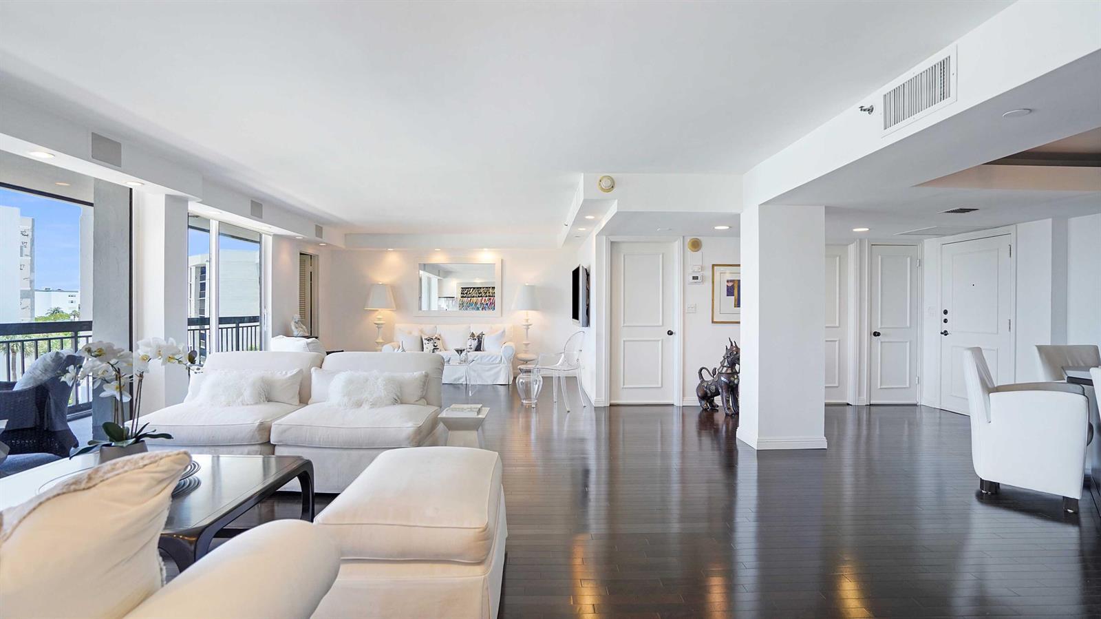 A bright, open-concept living room features white furniture, dark hardwood floors, and a balcony view — 2697 N Ocean Boulevard # 505, Boca Raton FL 33431, BOCA RATON, FL