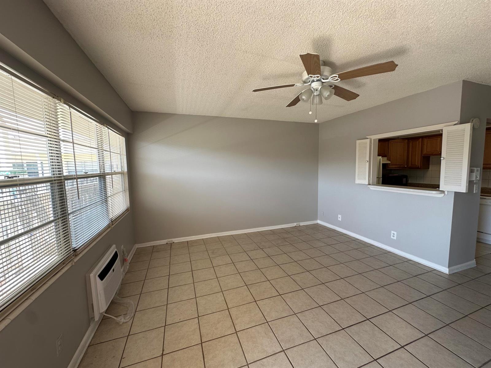 An empty room with gray walls, tile flooring, a ceiling fan, and a window pass-through — 119 Dorset # 119, Boca Raton FL 33434, BOCA RATON, FL