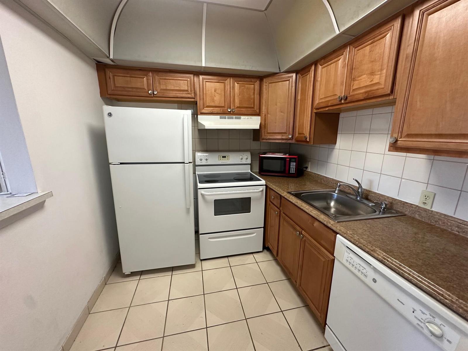A kitchen features wood cabinets, white appliances, a tiled backsplash, and a tiled floor — 119 Dorset # 119, Boca Raton FL 33434, BOCA RATON, FL