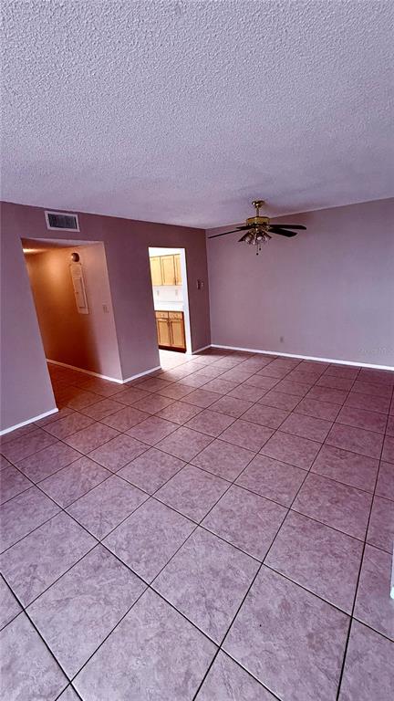 A room with light-colored tile flooring, a ceiling fan, and a doorway leading to a kitchen — 6519 W NEWBERRY ROAD UNIT 912, GAINESVILLE, FL