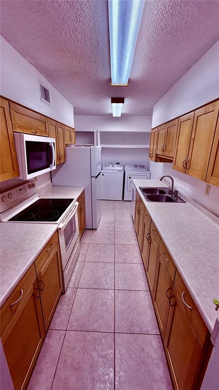 A galley-style kitchen features light wood cabinets, white countertops, and a laundry area at the end — 6519 W NEWBERRY ROAD UNIT 912, GAINESVILLE, FL
