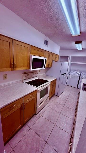 A kitchen features light wood cabinets, white appliances, and tile flooring — 6519 W NEWBERRY ROAD UNIT 912, GAINESVILLE, FL
