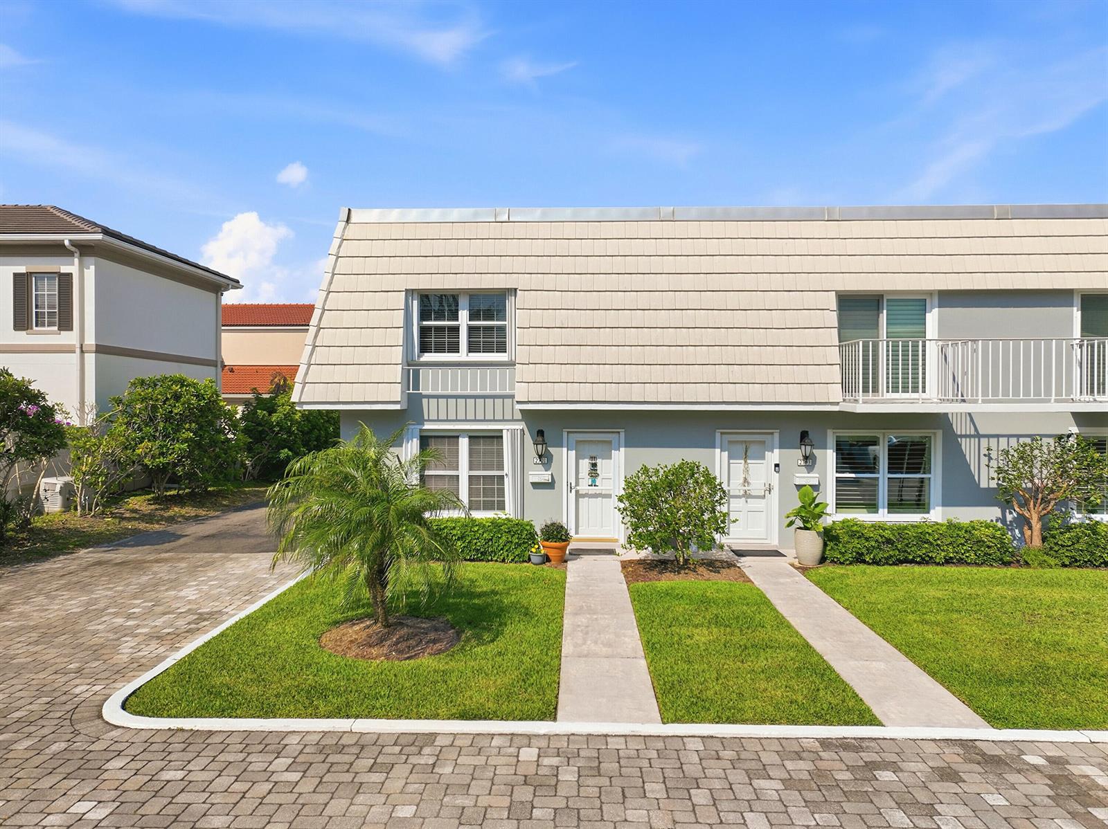A two-story townhouse exterior features a light-colored mansard roof, gray siding, and paved walkways — 2701 Ocean Drive # 1a, Vero Beach FL 32963, VERO BEACH, FL