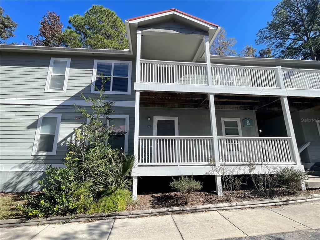 A two-story building features gray horizontal siding, white railings, and a covered ground-level porch — 2905 SW ARCHER ROAD UNIT S4022, GAINESVILLE, FL