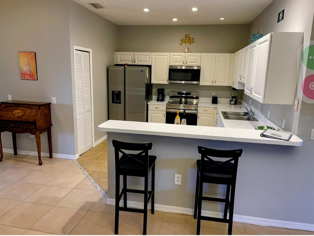 A kitchen with white cabinets, stainless steel appliances, and a breakfast bar with two stools — 3143 SUN LAKE COURT UNIT B, KISSIMMEE, FL
