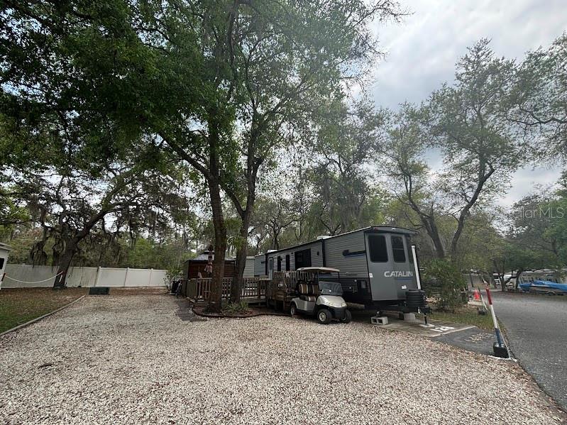 A gray Catalina travel trailer is parked on a gravel lot beneath large trees — 14403 252ND COURT ROAD NE UNIT 128, FORT MC COY, FL