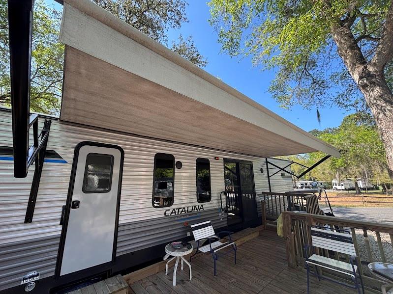 The exterior of a Catalina travel trailer features an extended awning and a wooden deck — 14403 252ND COURT ROAD NE UNIT 128, FORT MC COY, FL
