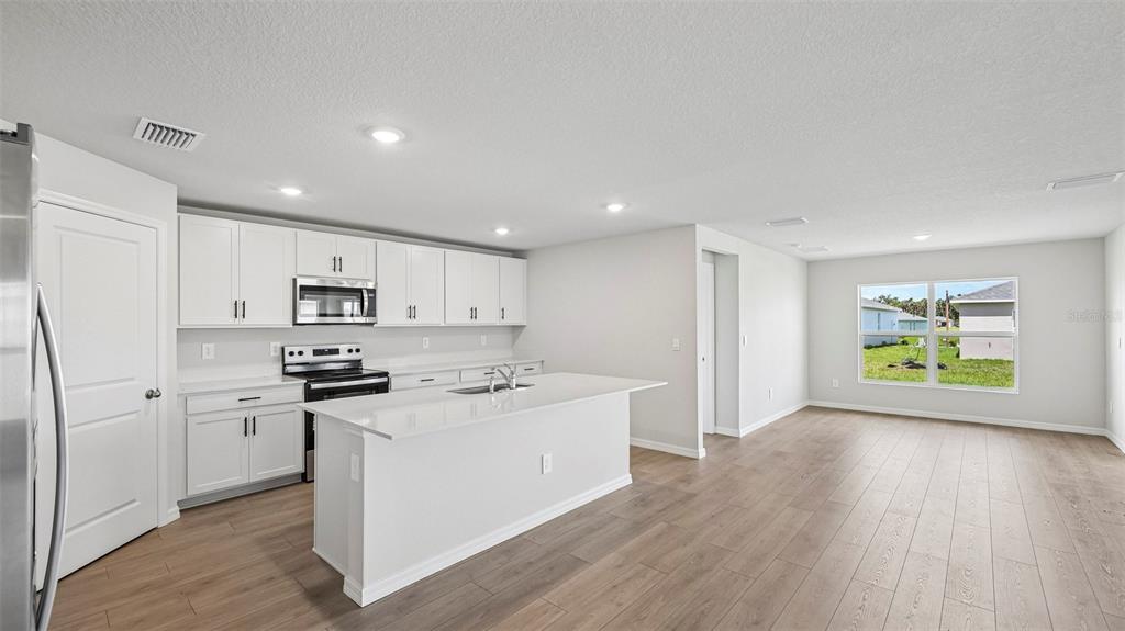 A modern kitchen with white cabinets, a central island, and light wood-look flooring — 17521 WHISKEY CREEK TRAIL, PARRISH, FL