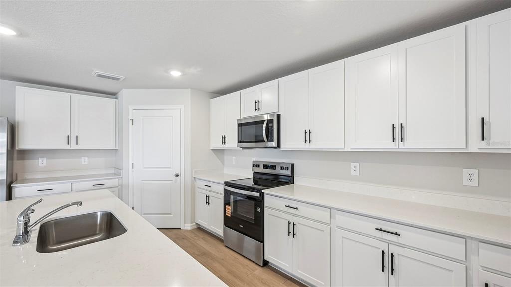 A kitchen features white cabinets, stainless steel appliances, and light-colored countertops — 17521 WHISKEY CREEK TRAIL, PARRISH, FL