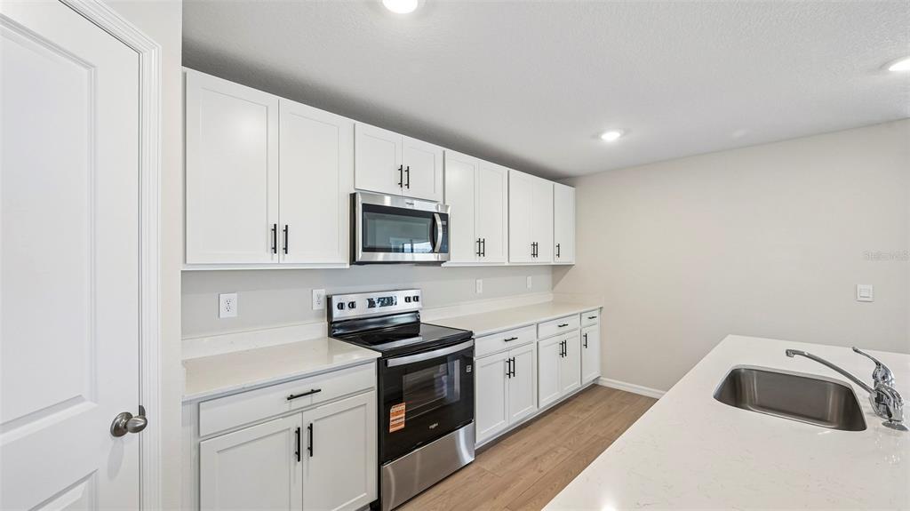 A kitchen with white cabinets, stainless steel appliances, and a quartz-topped island — 17521 WHISKEY CREEK TRAIL, PARRISH, FL