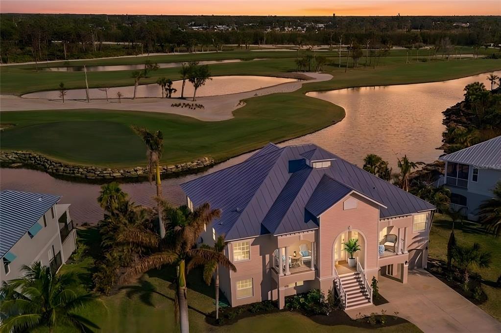 An aerial view of a pink house with a blue metal roof near a golf course — 10030 EAGLE PRESERVE DRIVE, ENGLEWOOD, FL