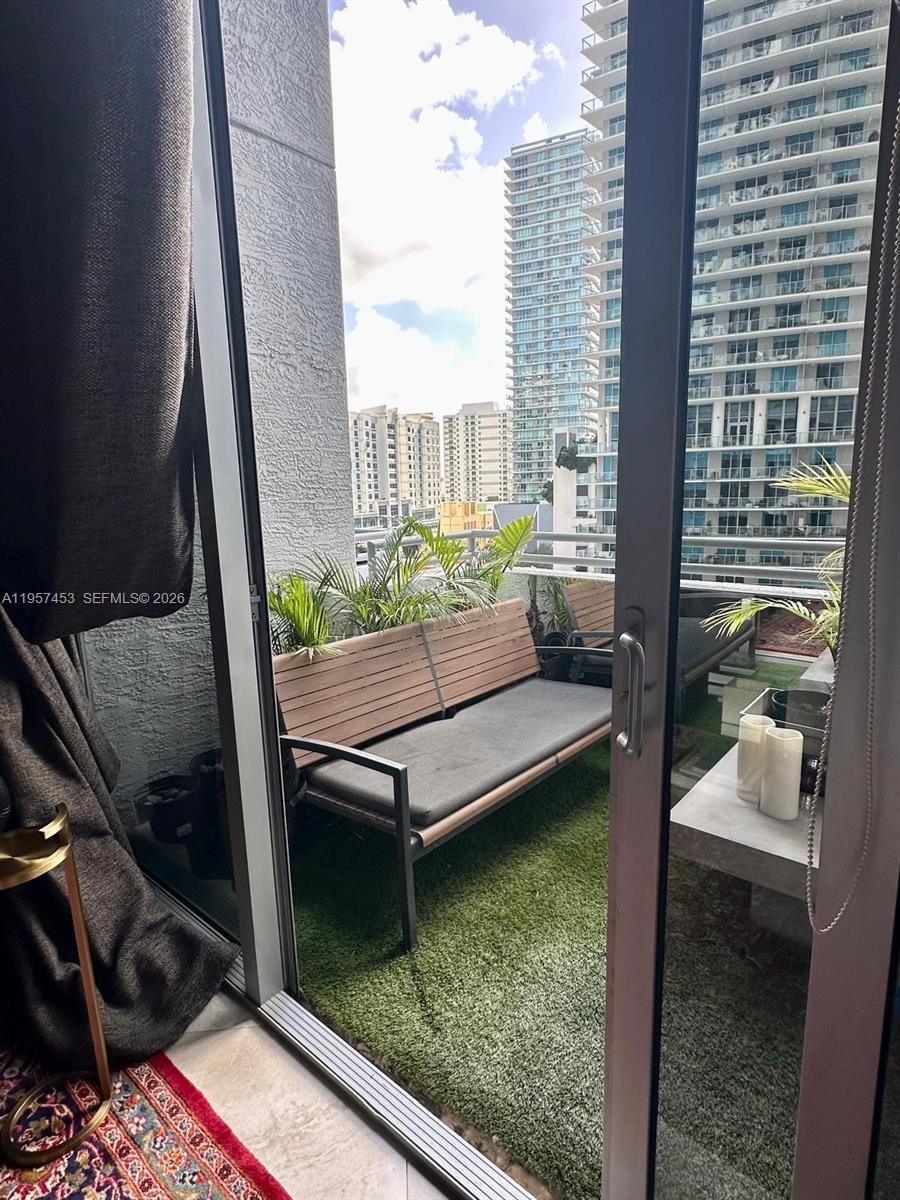 A balcony with artificial turf, a wooden bench, and potted plants overlooks city high-rise buildings — 1050 Brickell Ave # 818, Miami FL 33131, MIAMI, FL