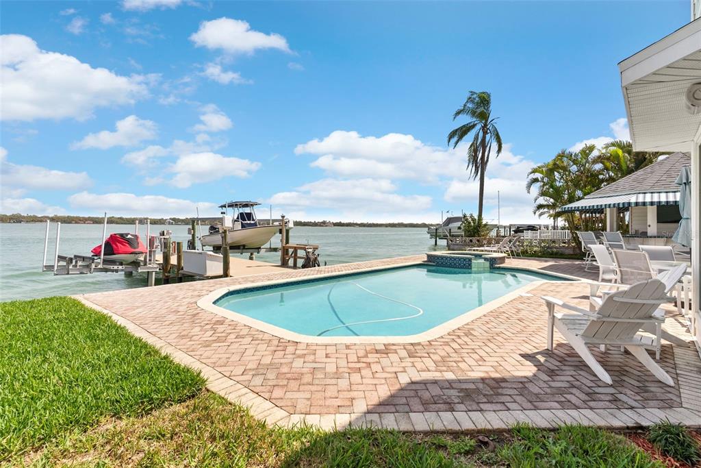 A swimming pool and patio overlook a waterfront dock with a boat and jet ski — 11445 9TH STREET E, TREASURE ISLAND, FL