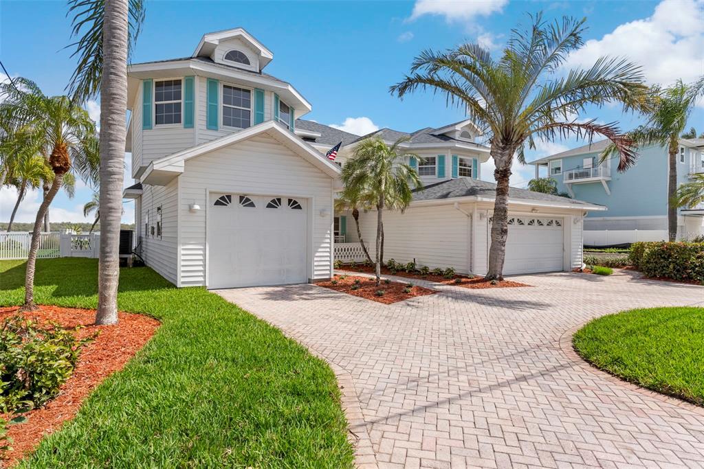 A two-story white house with teal shutters features two garages and palm trees outside — 11445 9TH STREET E, TREASURE ISLAND, FL