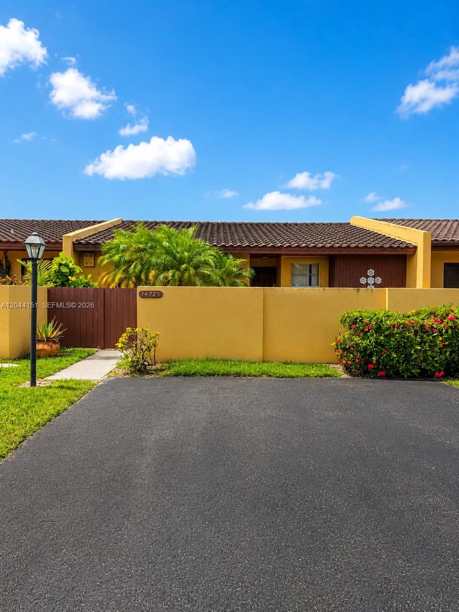 A yellow exterior wall with a brown fence and a palm tree under a blue sky — 14725 SW 86th Ln, Miami FL 33193, MIAMI, FL