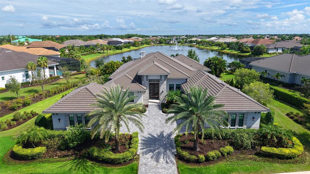 An aerial view of a single-story house with a tiled roof, palm trees, and driveway — 8339 LUCERNE LOOP, BRADENTON, FL