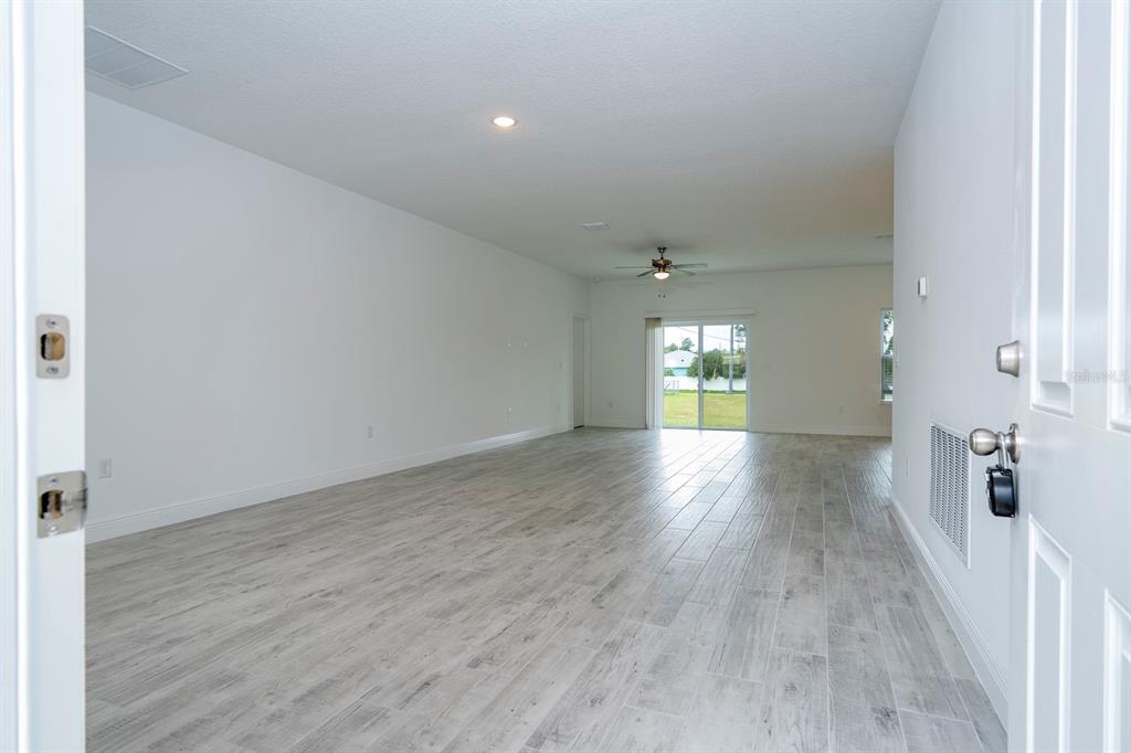 An empty living room features light wood-look tile flooring, white walls, and sliding glass doors — 7764 N DARBY DRIVE, CITRUS SPRINGS, FL