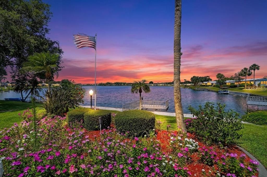 A view of a lake at sunset with a flag, palm trees, and flower beds — 8469 IMPERIAL LAKES CIRCLE, PALMETTO, FL