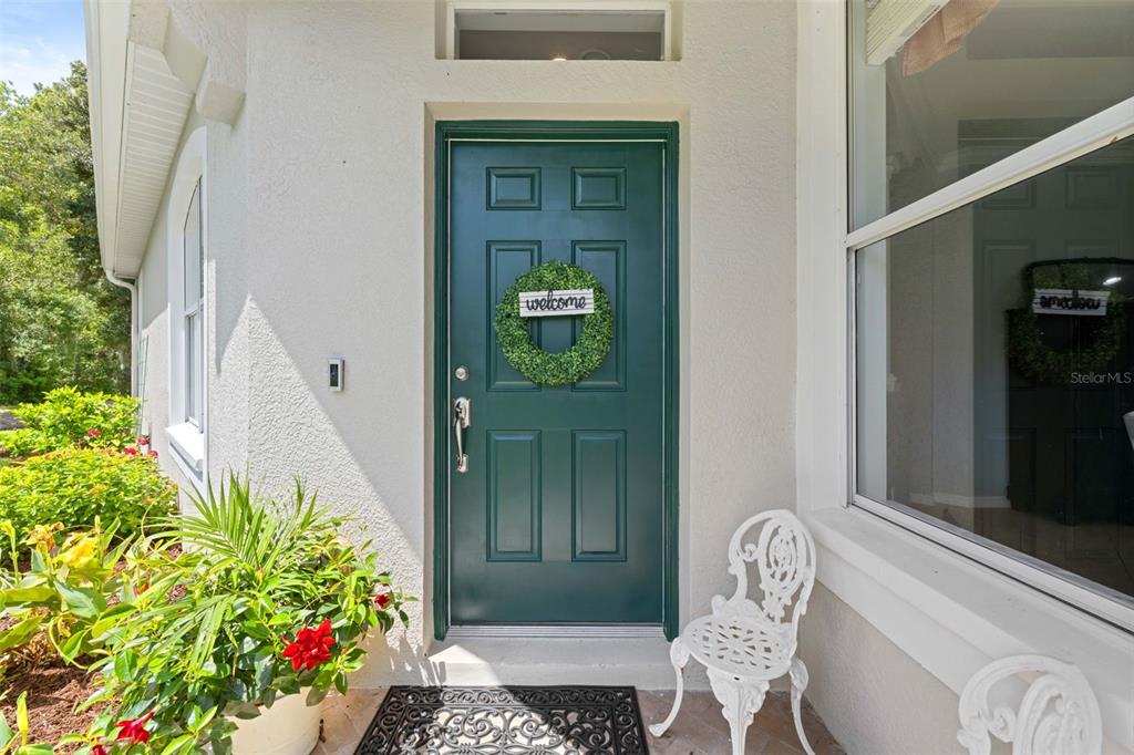 A green front door with a wreath stands on a porch next to a chair — 3348 CHAPEL CREEK CIRCLE, WESLEY CHAPEL, FL