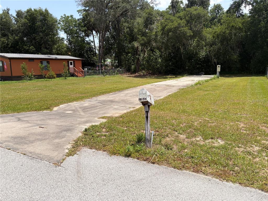 A long concrete driveway leads toward an orange mobile home on a grassy lot — 11047 SE 66TH TERRACE, BELLEVIEW, FL