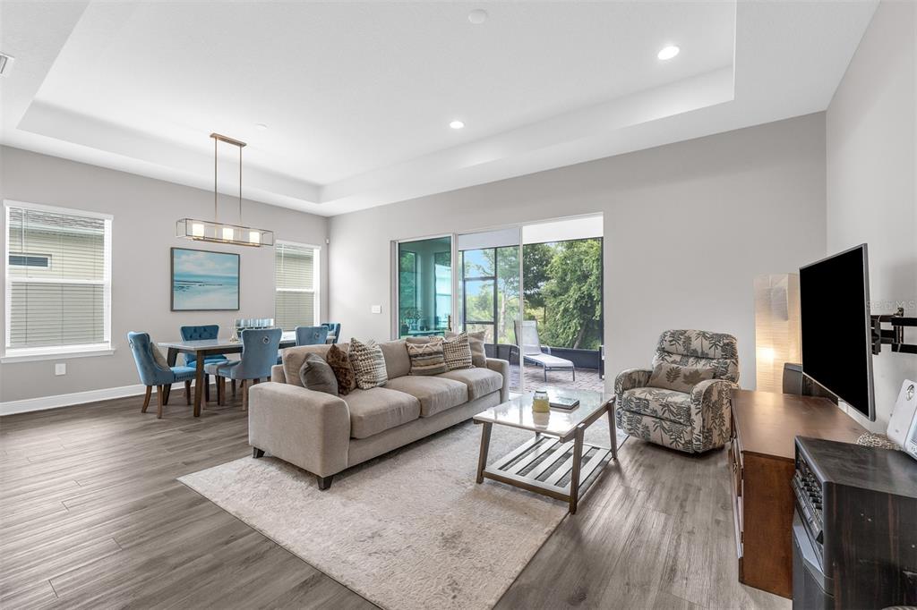 An open-concept living and dining area features wood-look flooring, a tray ceiling, and sliding glass doors — 2103 LIMESTONE TRAIL, KISSIMMEE, FL