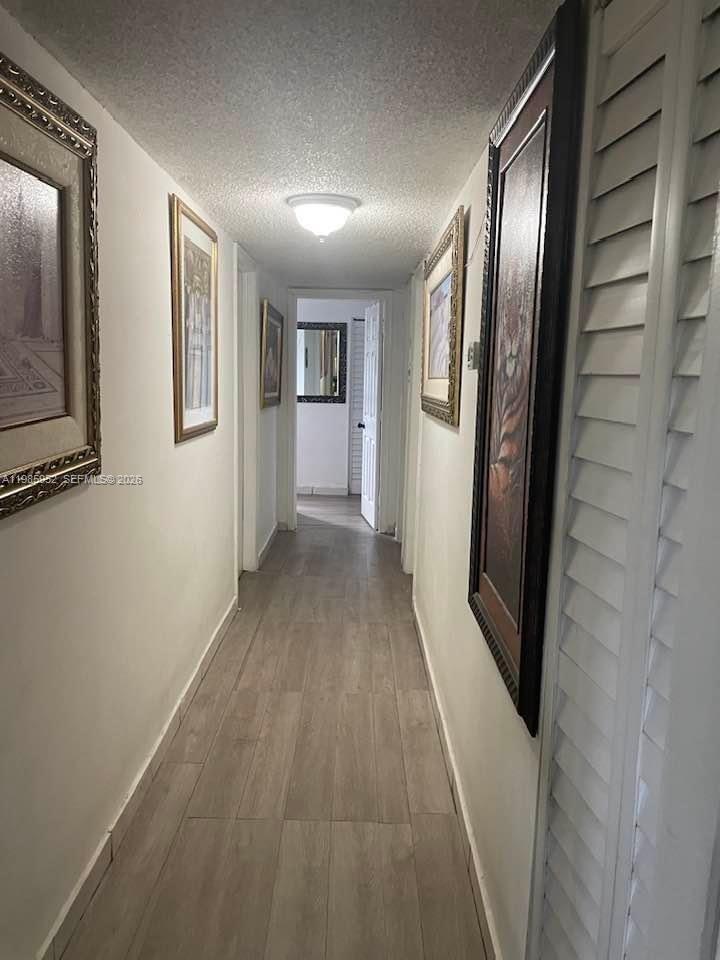 A narrow hallway features light wood-look flooring, white walls, and several framed wall art pieces — 6901 SW 147th Ave # 2E, Miami FL 33193, MIAMI, FL