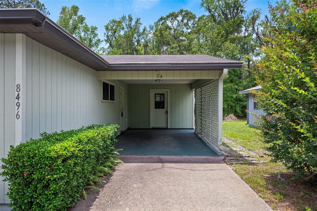 A light green house features a concrete driveway leading to a covered carport entrance — 8496 NW 37TH TERRACE, GAINESVILLE, FL