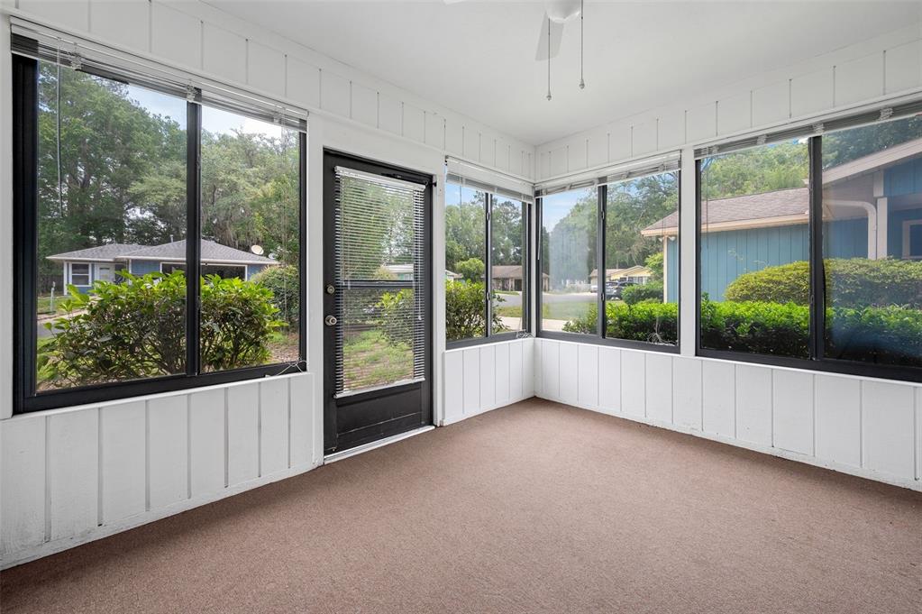 A sunroom with white vertical paneling, brown carpeting, large windows, and a black exterior door — 8496 NW 37TH TERRACE, GAINESVILLE, FL