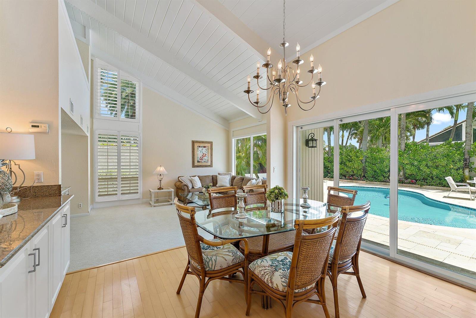 A dining area with a glass table and rattan chairs opens to a backyard pool — 107 Mako Lane, Jupiter FL 33477, JUPITER, FL