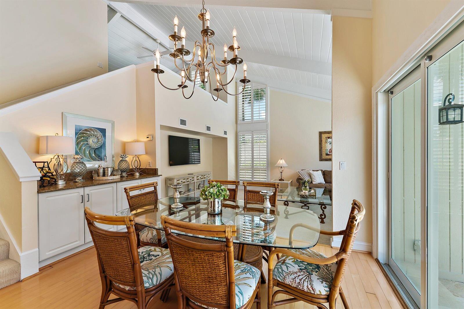A dining room features a glass table, wicker chairs, a chandelier, and a built-in sideboard — 107 Mako Lane, Jupiter FL 33477, JUPITER, FL