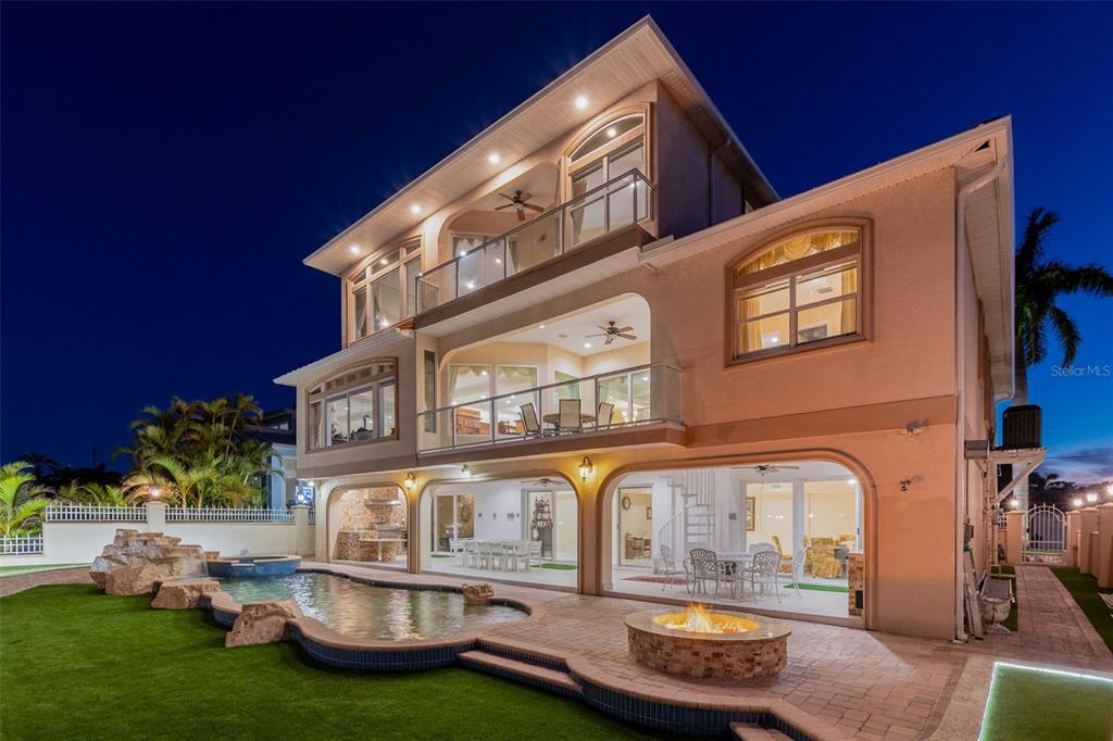 A three-story house exterior at night featuring a swimming pool, fire pit, and balconies — 1203 BAY DRIVE, BELLEAIR BEACH, FL