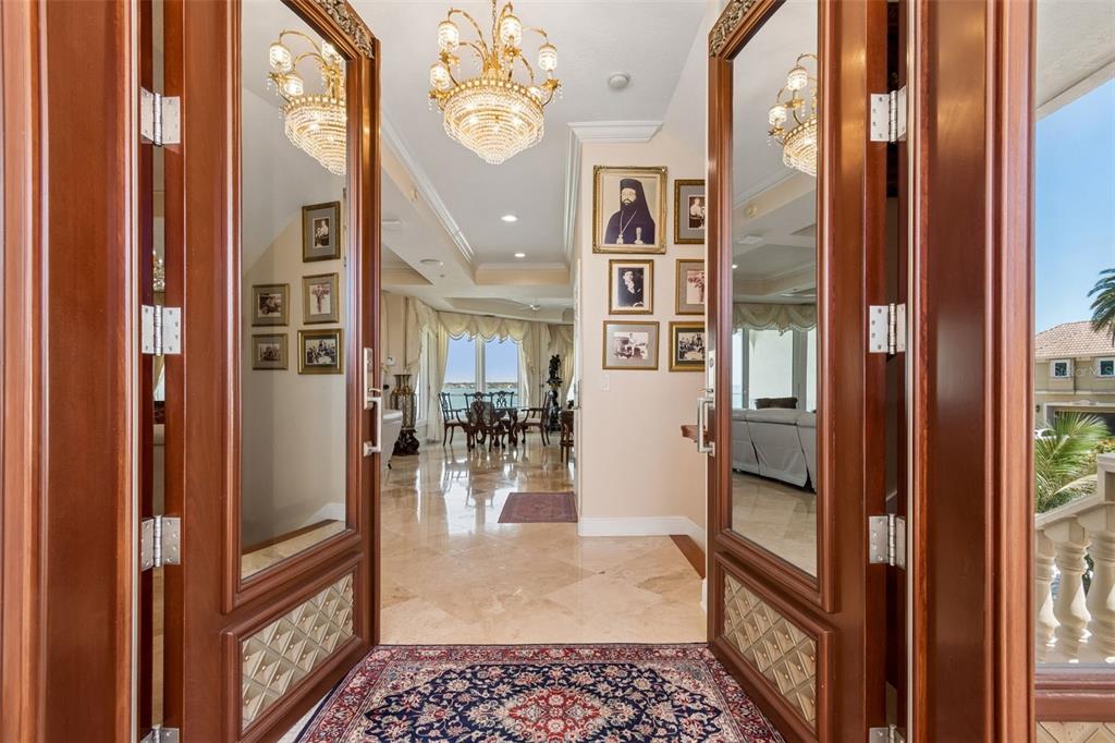 A view through double wooden doors into a foyer with a chandelier and marble floors — 1203 BAY DRIVE, BELLEAIR BEACH, FL