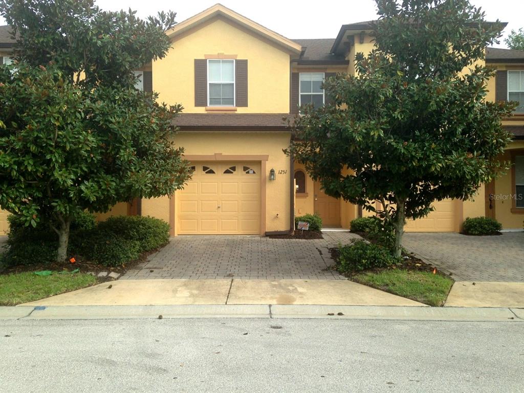 A two-story yellow stucco townhouse with a single-car garage and two trees in front — 1251 LONG OAK WAY, SANFORD, FL